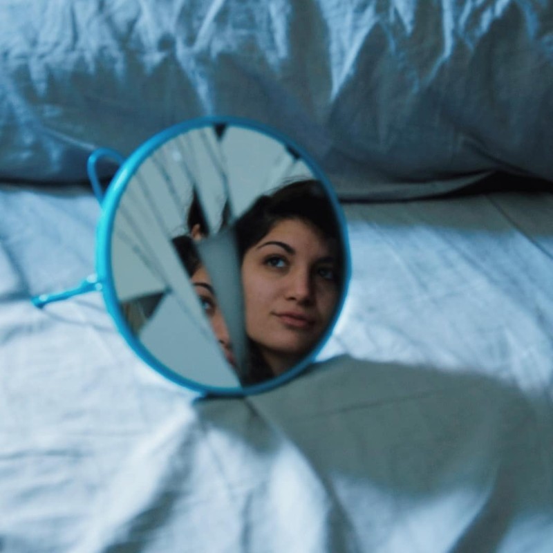 il volto di Veronica riflesso su uno specchio rotto e adagiato su un letto sfatto